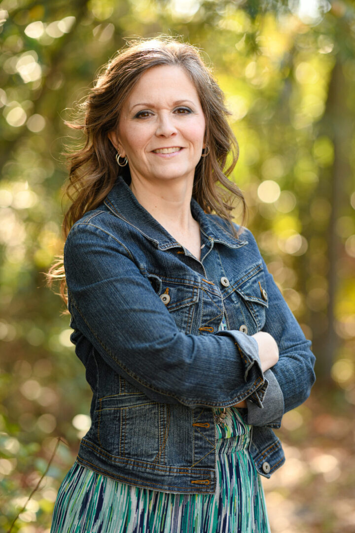 A woman standing in the woods with her arms crossed.